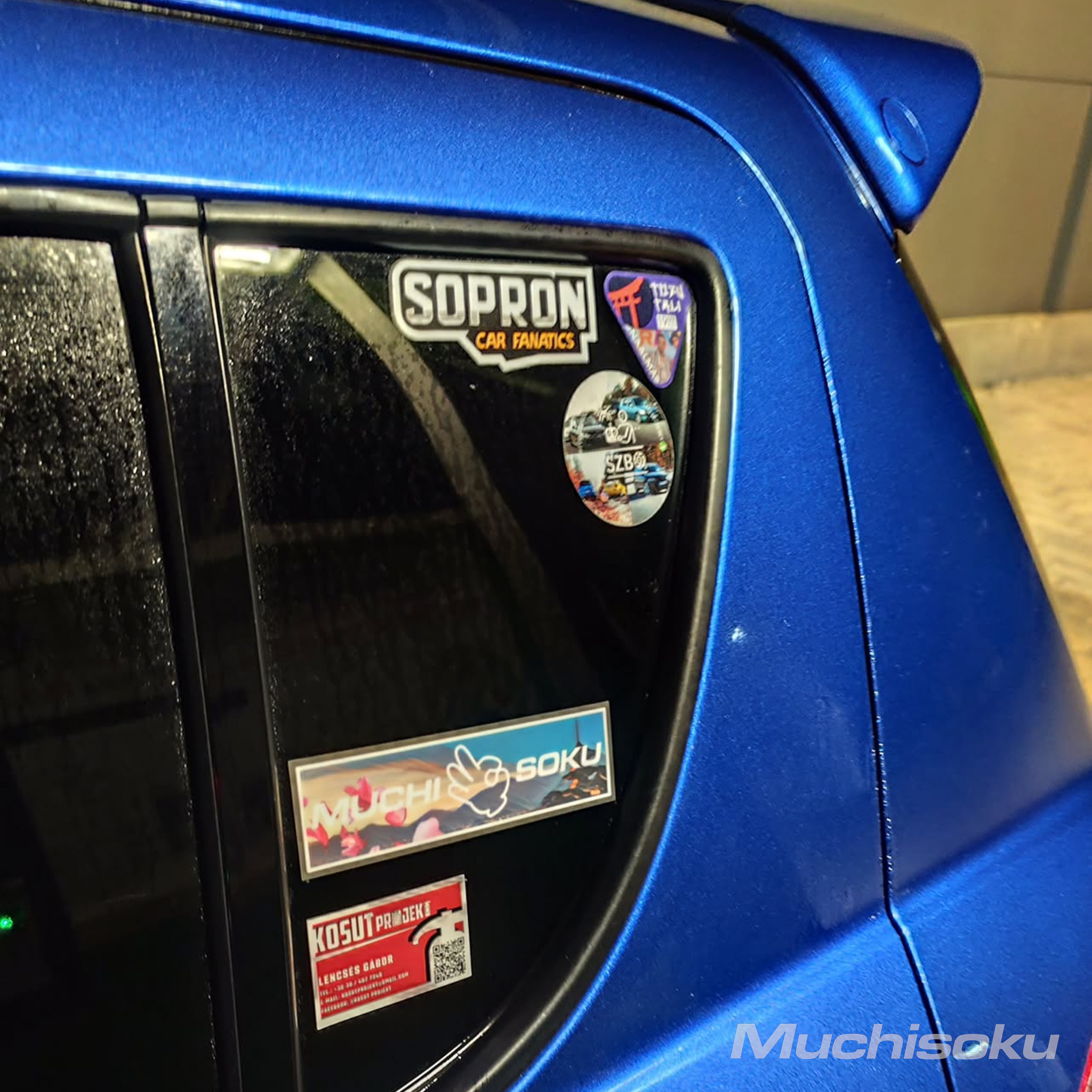 Muchisoku Fuji echo slap sticker next to a bunch of other stickers on a blue Suzuki Swift Sport.