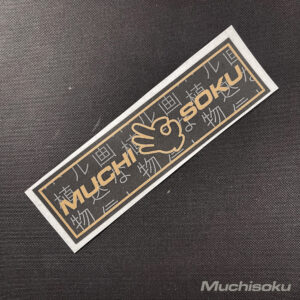 Concrete royalty slap sticker on dark background. Features the Muchisoku typo and an OK hand signal in gold.